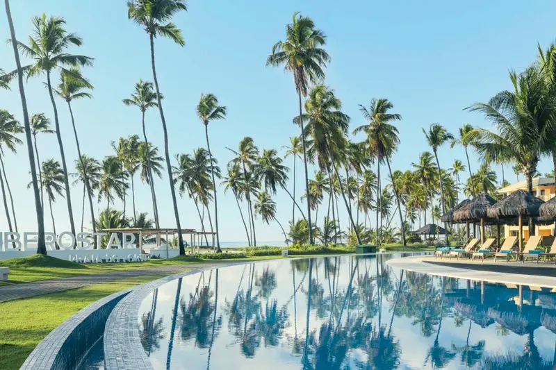 Piscina de borda infinita refletindo os coqueiros, com o letreiro Iberostar ao fundo